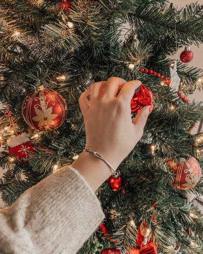 A man sitting on the floor next to a Christmas tree, opening a gift.